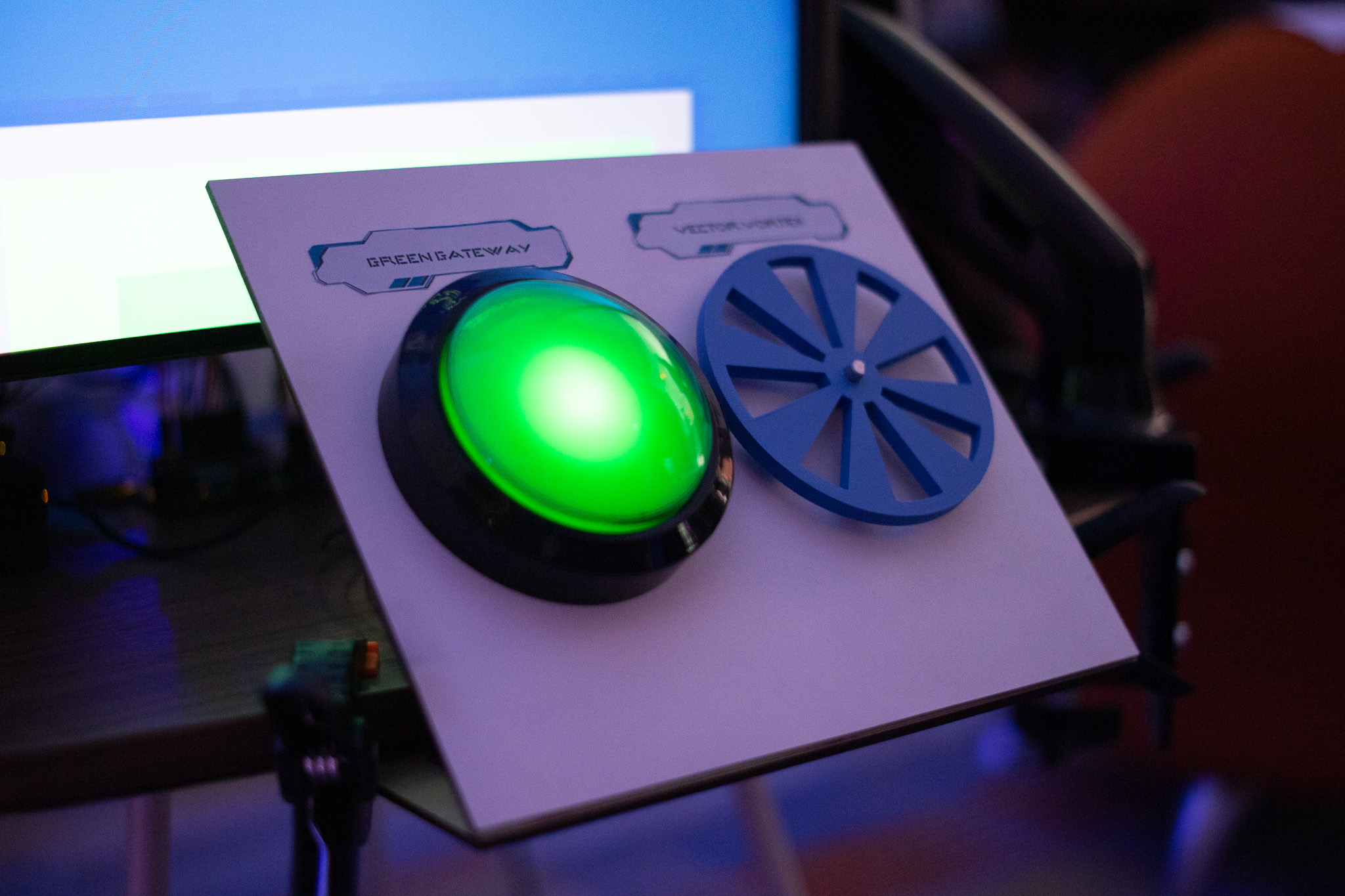 A large glowing green button and a blue spinner, mounted on a white panel. They are labeled as the Green Gateway and the Vector Vortex in a futuristic title.